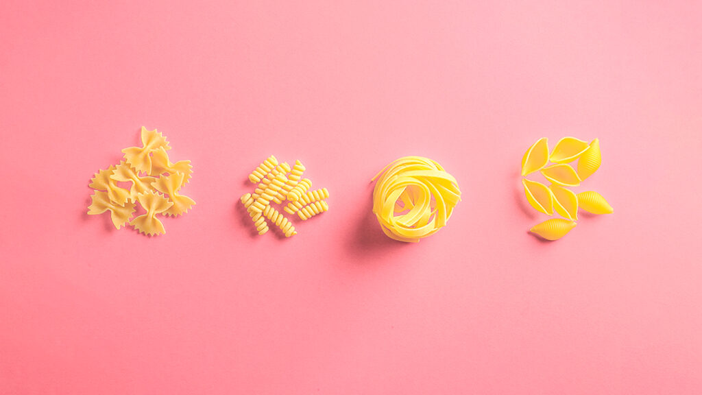 Assortment of pasta on a pink background illustrating diversity.